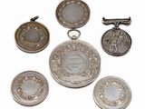six silver coins and a silver pendant on a white background
