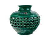un vase vert percé de trous sur fond blanc