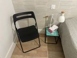 a black folding chair next to a bed in a small room