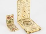 un cadran solaire ancien, accompagné d'une boussole et d'un livre, posé sur une surface blanche