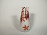 a white vase with red leaves on it sitting on a table