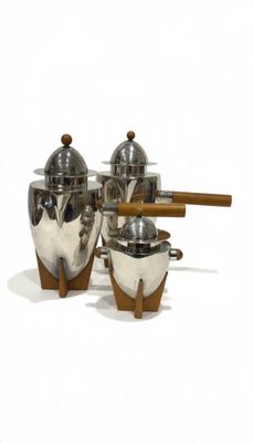 three silver pots and a wooden spoon on a white surface