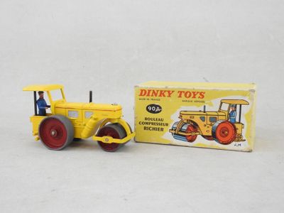 un petit tracteur jaune avec une boîte de Dinky Toys posée sur une surface blanche