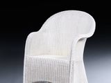 a white wicker chair on a grey floor with a black background