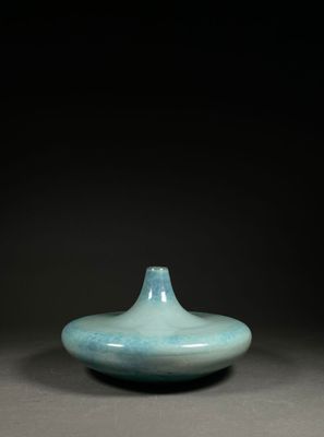 un vase bleu posé sur une table, devant un fond noir