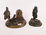 deux figurines en bronze représentant des hommes et une horloge posées sur une surface blanche