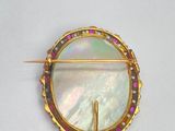 an image of a broochle with a white shell and pink and green stones