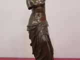 bronze statue of a woman holding a vase on a pink surface