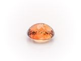 a close up of an orange sapphire stone on a white surface