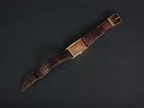 a brown leather watch strap with a gold buckle on a black background