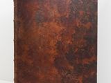 an old book with a brown cover sitting on a white surface