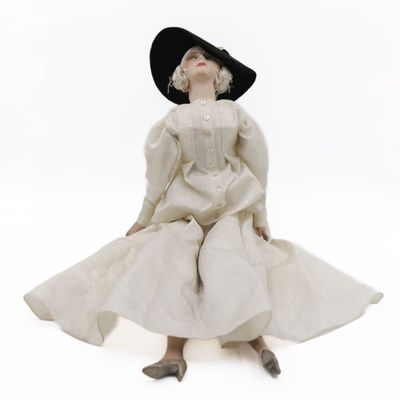 a woman in a white dress and black hat sitting on the floor