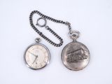 une montre de poche en argent avec une chaîne, posée sur une surface blanche
