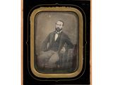 une vieille photo d'un homme en costume assis sur une chaise