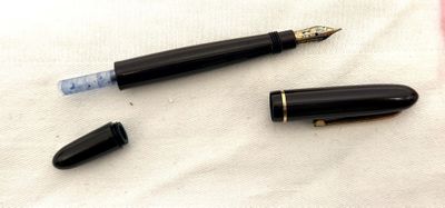 un stylo noir et un stylo à plume noir posés sur un tissu blanc