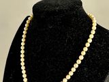 a white pearl necklace on a black mannequin with a gold clasp