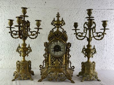 trois bougeoirs en laiton et une horloge posés sur une table