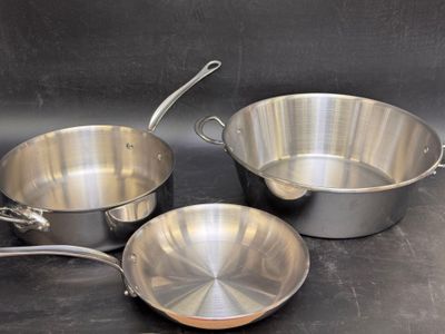 trois casseroles et poêles en acier inoxydable posées sur un plan de travail noir
