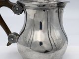 an antique silver teapot with a wooden handle on a white surface