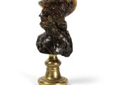 un buste antique en bronze représentant un homme coiffé d'un chapeau, posé sur un socle
