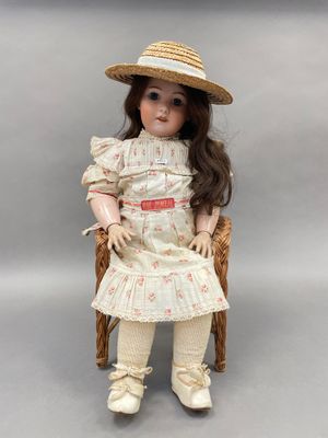 une vieille poupée assise sur une chaise, coiffée d'un chapeau et vêtue d'une robe