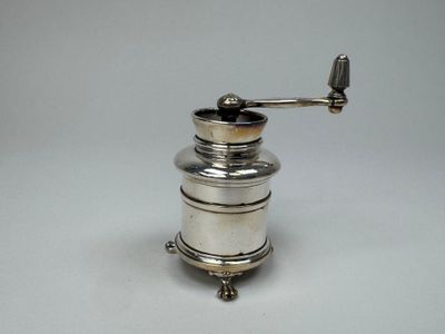 Moulin à café plaqué argent posé sur une surface blanche, avec un fond blanc