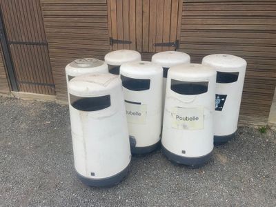 four white trash cans are lined up in front of a garage door