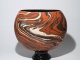 an orange and black vase sitting on a black stand