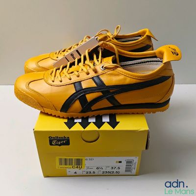 des baskets Onitsuka jaunes et noires posées sur une boîte jaune, elle-même posée sur une table blanche
