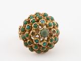 une image représentant une bague en or sertie de pierres vertes sur fond blanc