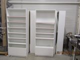 two tall white refrigerators in a room with a lot of shelves