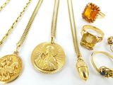 plusieurs colliers en or, bagues et pendentifs posés sur une surface blanche