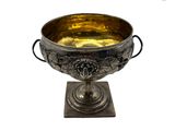 une coupe en argent posée sur un socle en métal, sur fond blanc