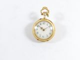 une petite montre de poche en or posée sur une surface blanche