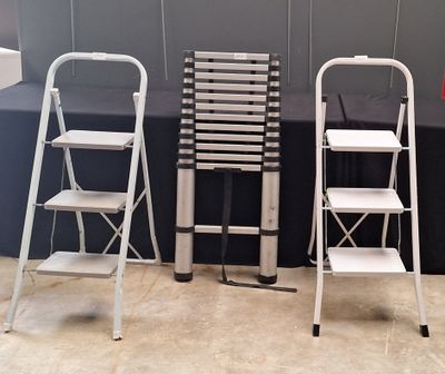 three metal ladders are lined up against a gray wall