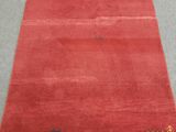 un tapis rouge posé sur un sol gris, bordé d'une frange blanche