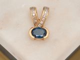 une photo d'un pendentif en saphir bleu et diamants posé sur une surface en marbre blanc