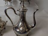 three silver teapots and two silver cups on a table