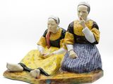 deux figurines représentant deux femmes assises sur un rocher, sur fond blanc