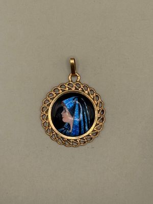 a close up of a gold plated pendant with a picture of a woman in a blue dress