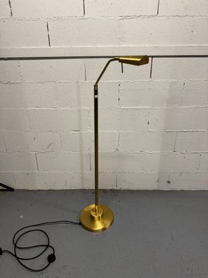 lampe sur pied en laiton plaqué, avec un cordon noir et un mur de briques blanches en arrière-plan