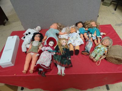 a lot of dolls sitting on a table with a red table cloth