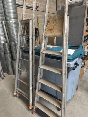 une pile d'échelles dans un garage, avec une poubelle bleue en arrière-plan