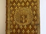 an old book with a gold cover sitting on a white surface