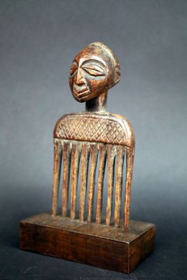 une image représentant un peigne en bois surmonté d'un visage sculpté