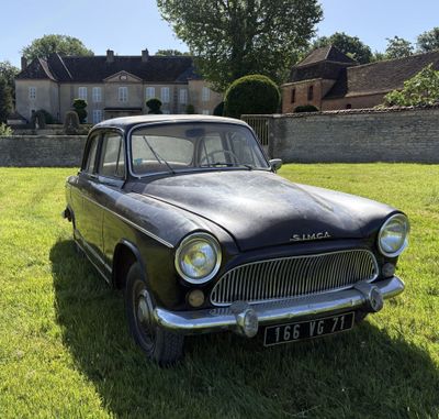 Une vieille voiture noire est garée dans l'herbe devant une maison.