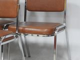 two brown leather chairs with chrome legs and a white wall
