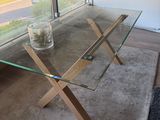 une table en verre avec des pieds en bois, sur laquelle se trouve un vase