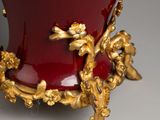 a red vase with a gold decoration on it