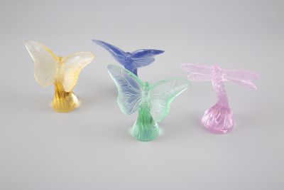 trois figurines en verre de couleurs et de formes différentes posées sur une surface blanche